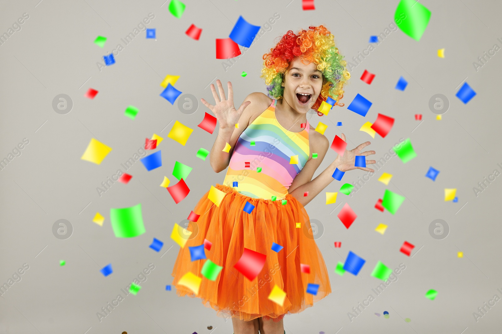 Image of Happy girl dressed like clown under falling confetti on grey background. Party time