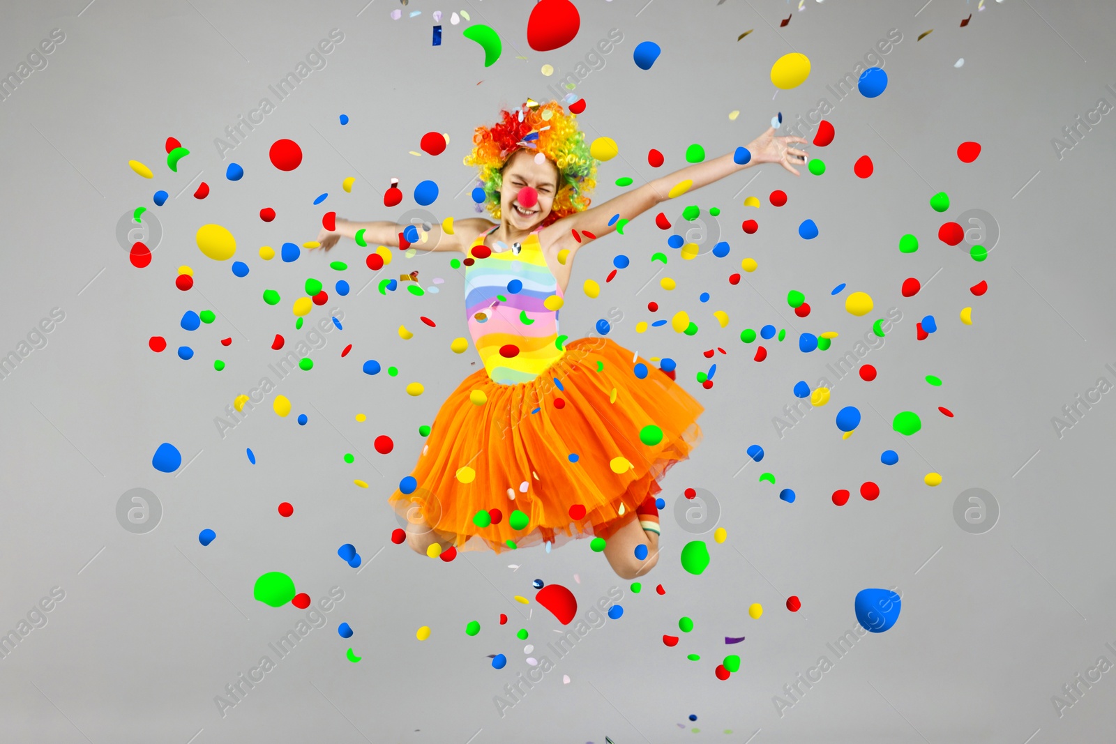 Image of Happy girl dressed like clown jumping under falling confetti on grey background. Party time