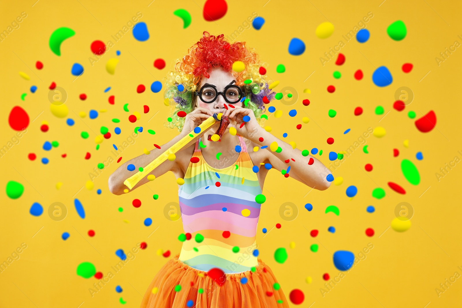 Image of Girl dressed like clown with party blowers under falling confetti on orange background