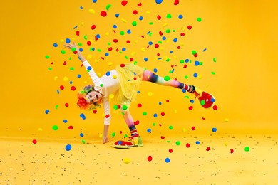 Image of Happy girl dressed like clown under falling confetti on orange background. Party time