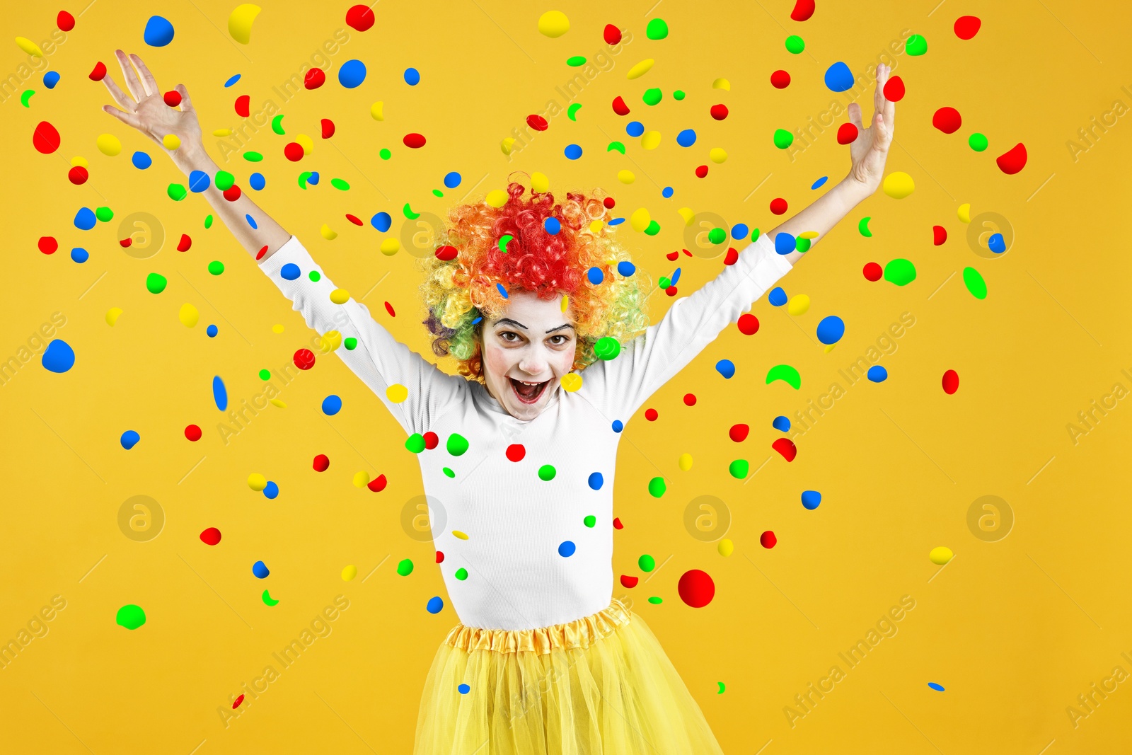 Image of Happy girl dressed like clown under falling confetti on orange background. Party time