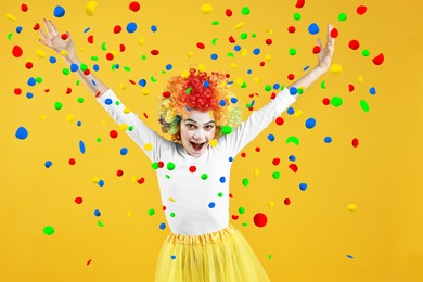 Image of Happy girl dressed like clown under falling confetti on orange background. Party time