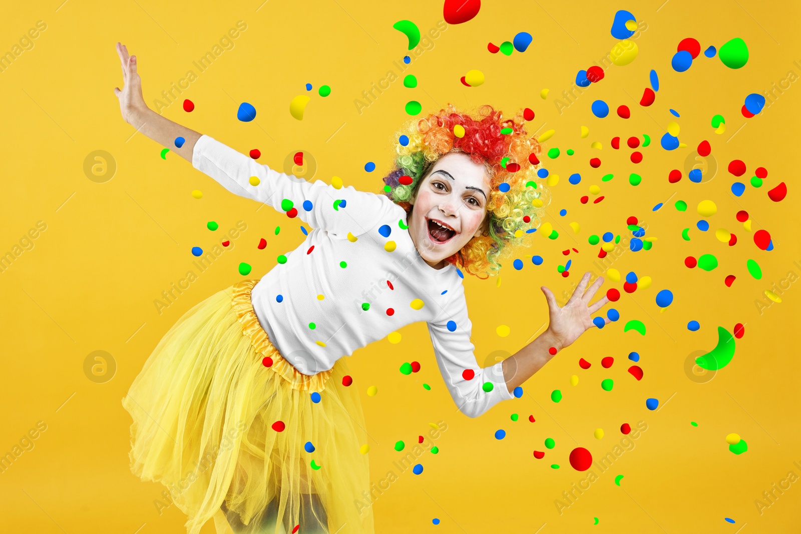 Image of Happy girl dressed like clown under falling confetti on orange background. Party time