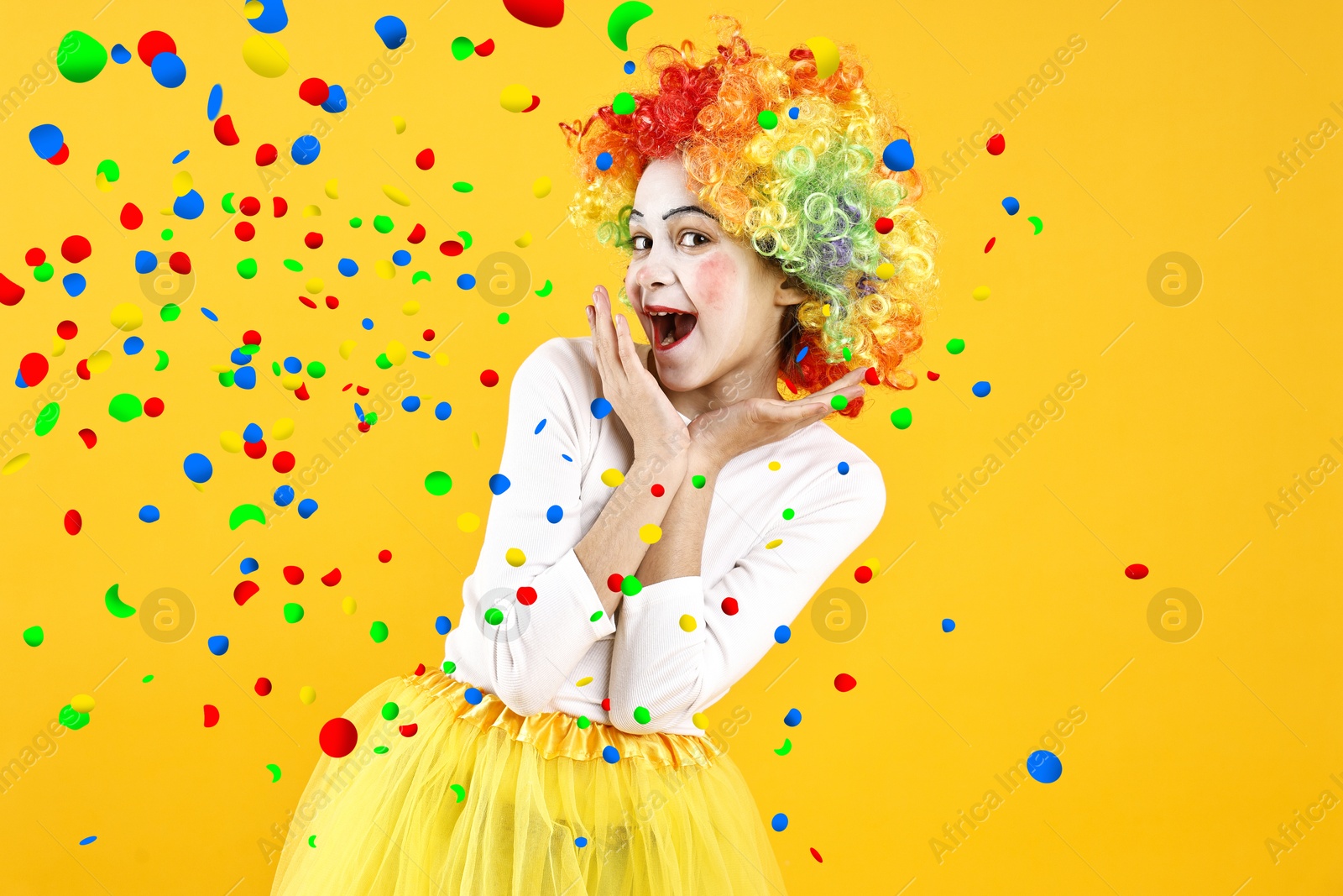 Image of Happy girl dressed like clown under falling confetti on orange background. Party time