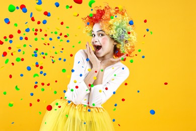 Image of Happy girl dressed like clown under falling confetti on orange background. Party time