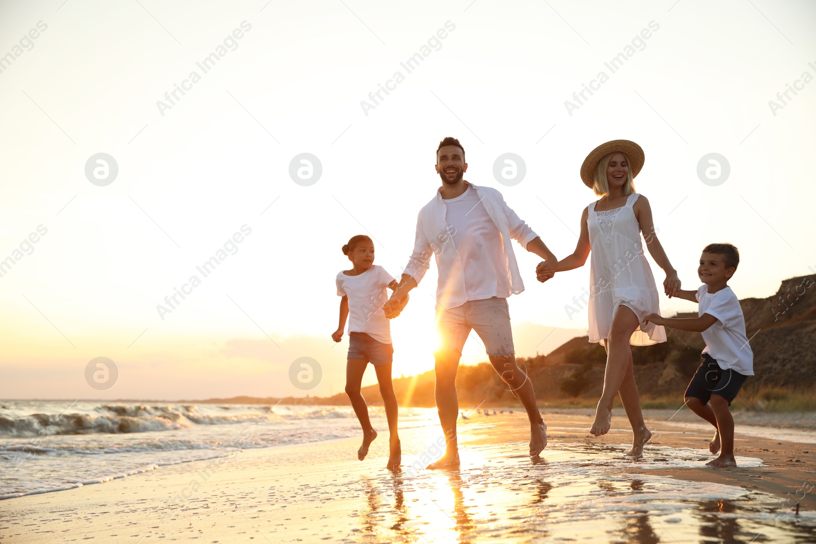 Photo of Happy family running on sandy beach near sea at sunset