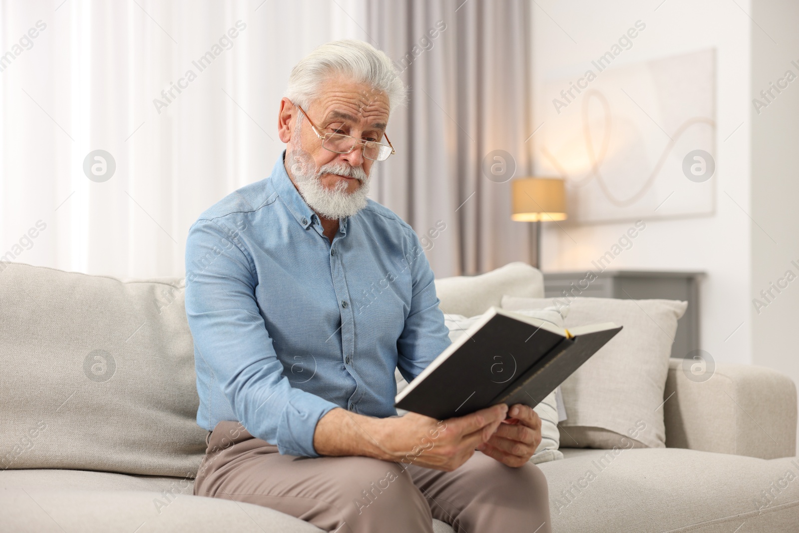 Photo of Handsome bearded man reading book on sofa indoors