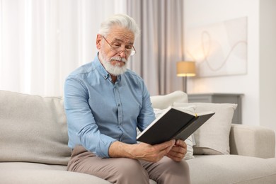 Photo of Handsome bearded man reading book on sofa indoors