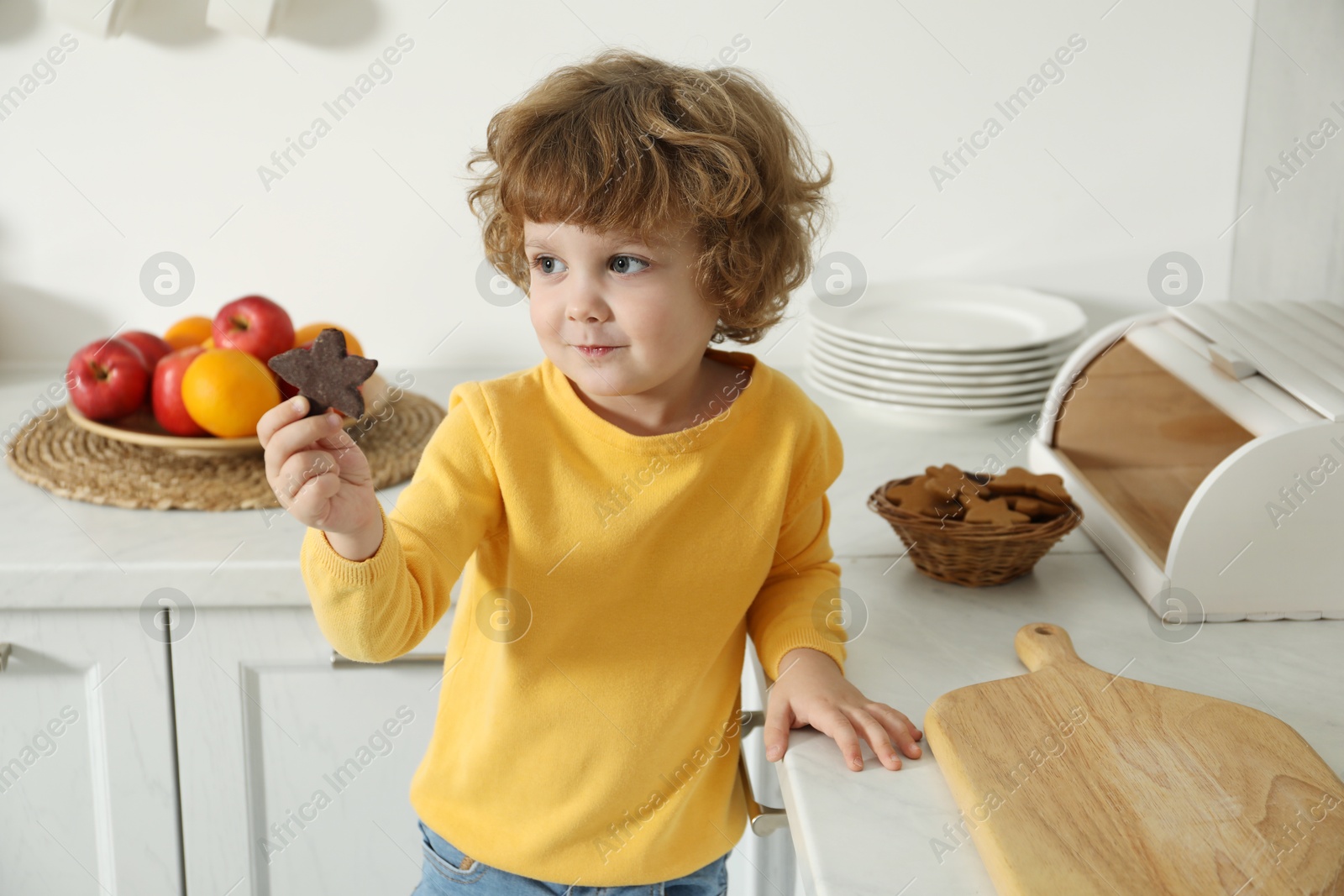 Photo of Little boy with cookie near countertop in kitchen