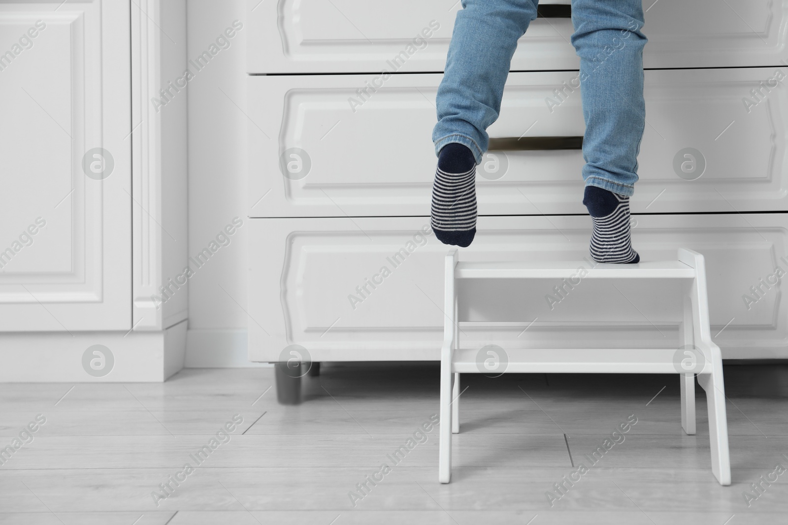 Photo of Little boy standing on step stool near chest of drawers at home, closeup