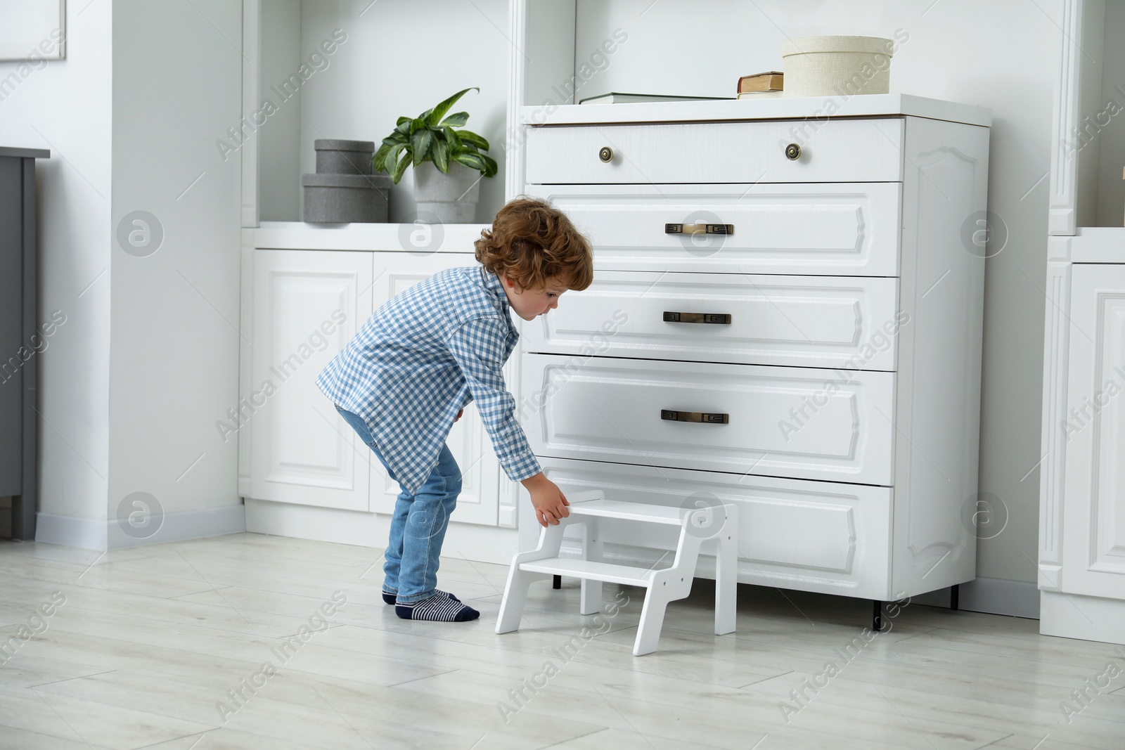 Photo of Little boy with step stool near chest of drawers at home