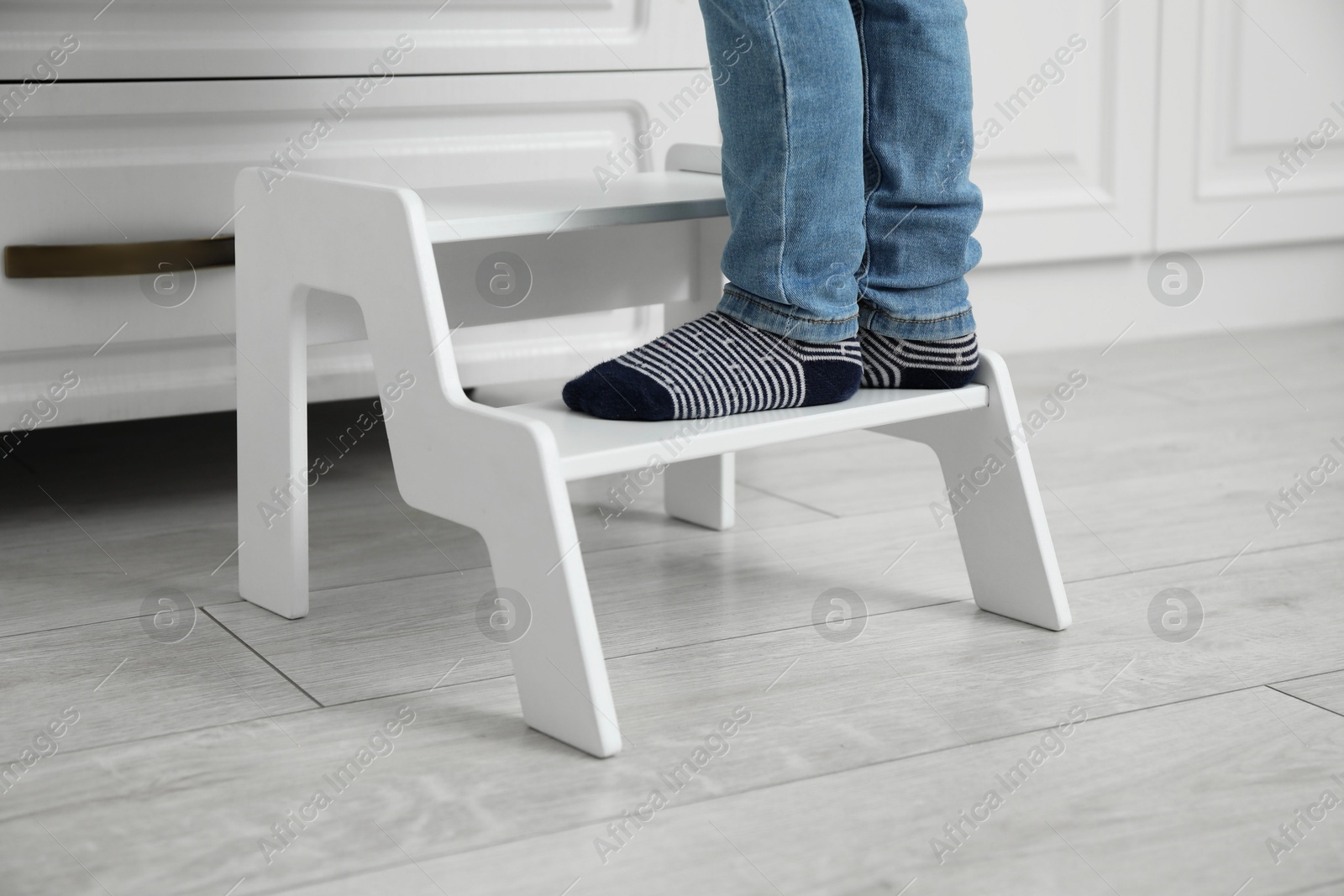 Photo of Little boy with step stool near chest of drawers at home, closeup