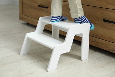 Photo of Little boy with step stool near chest of drawers at home, closeup