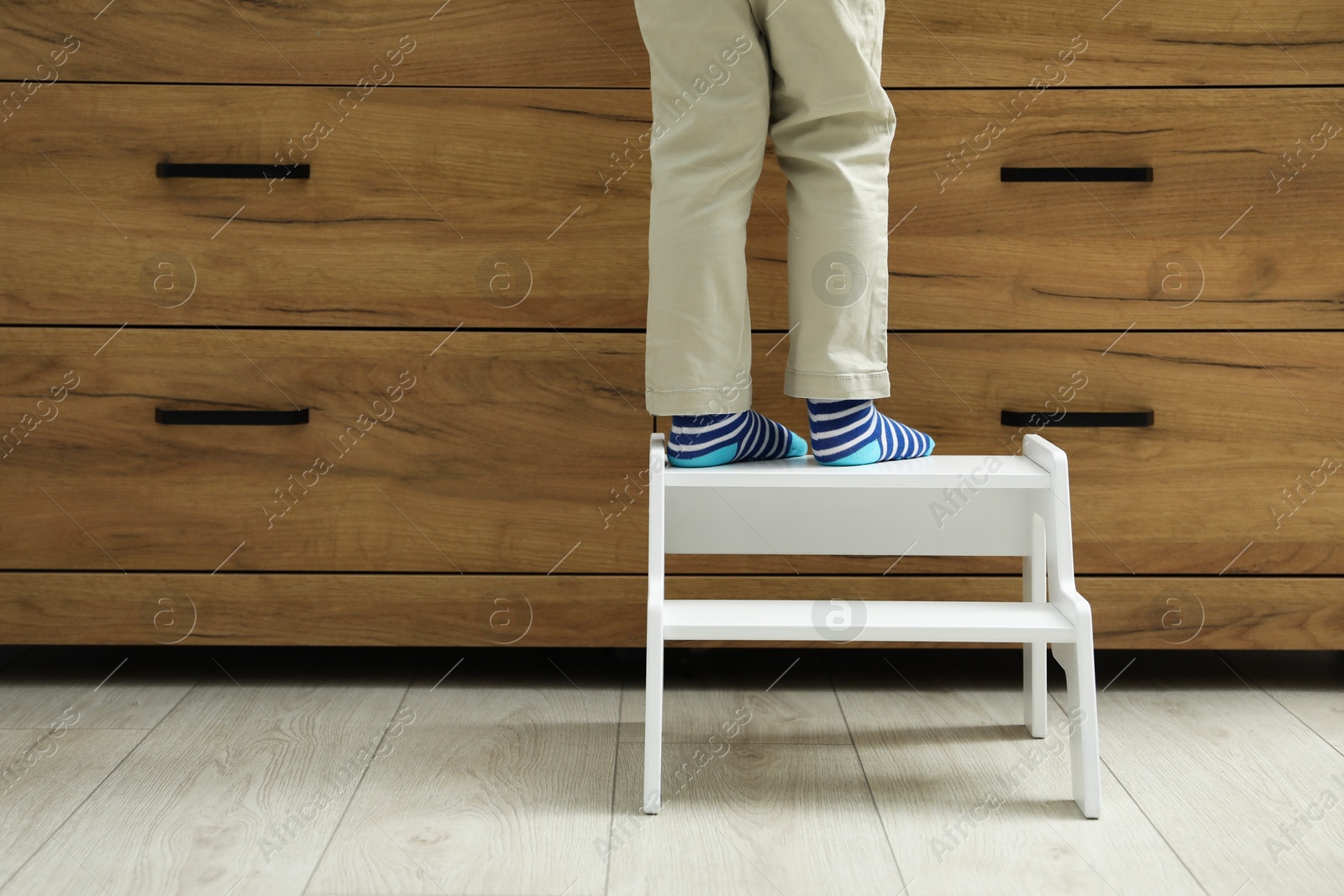 Photo of Little boy with step stool near chest of drawers at home, closeup