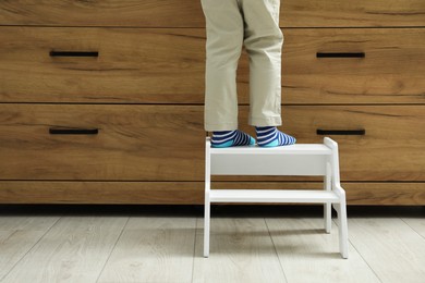 Photo of Little boy with step stool near chest of drawers at home, closeup