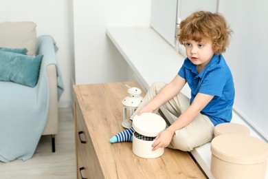 Photo of Little boy with boxes on window sill at home