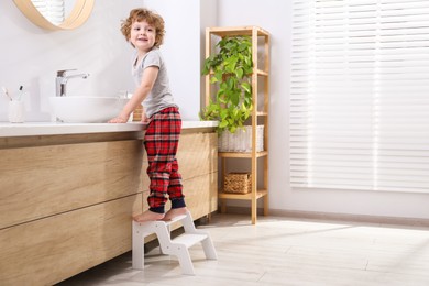 Little boy standing on step stool near bathroom vanity indoors