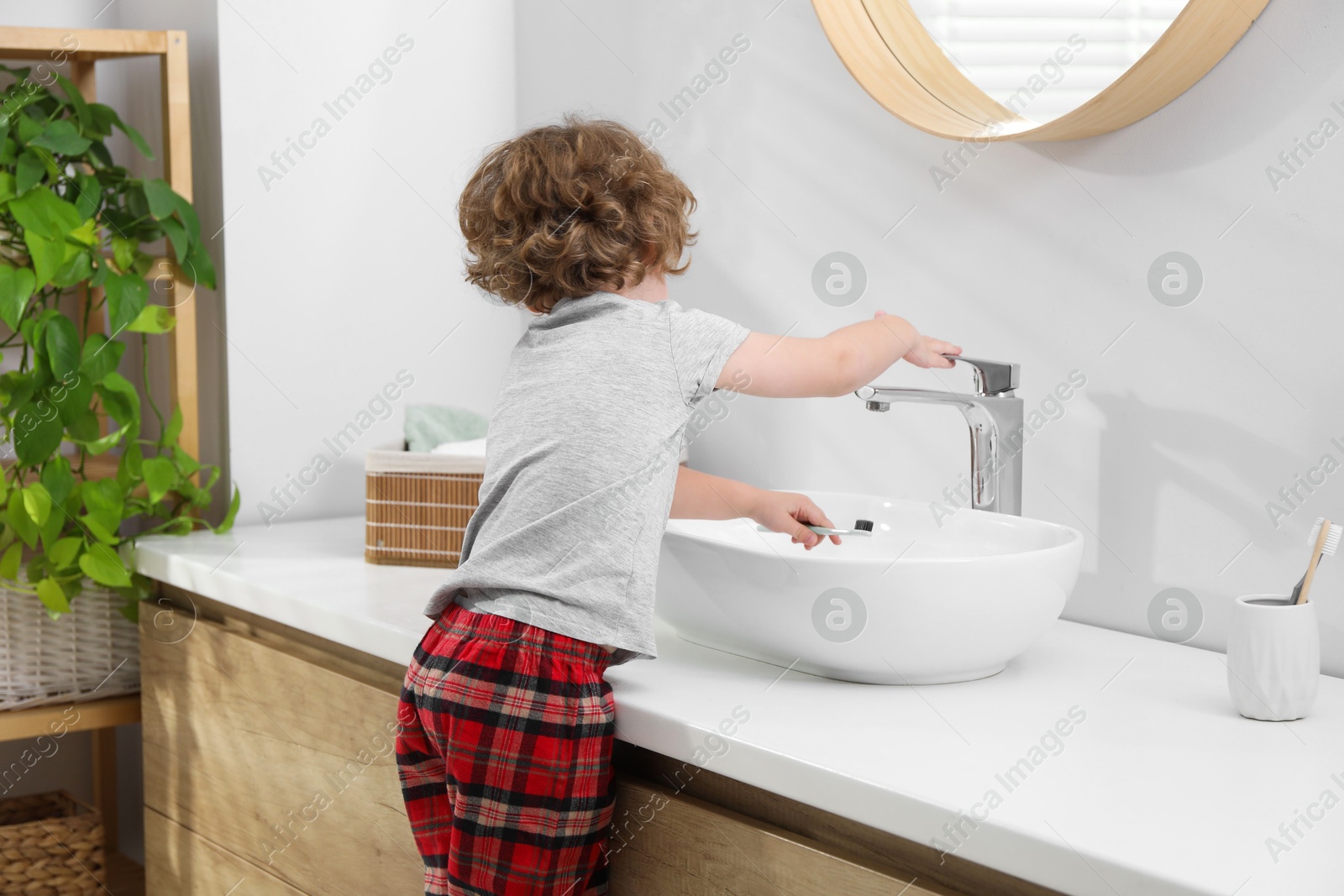 Photo of Little boy with toothbrush near bathroom vanity indoors