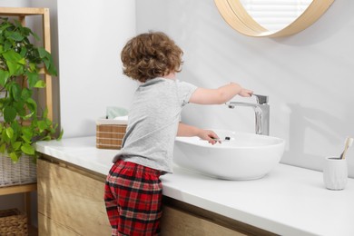 Little boy with toothbrush near bathroom vanity indoors