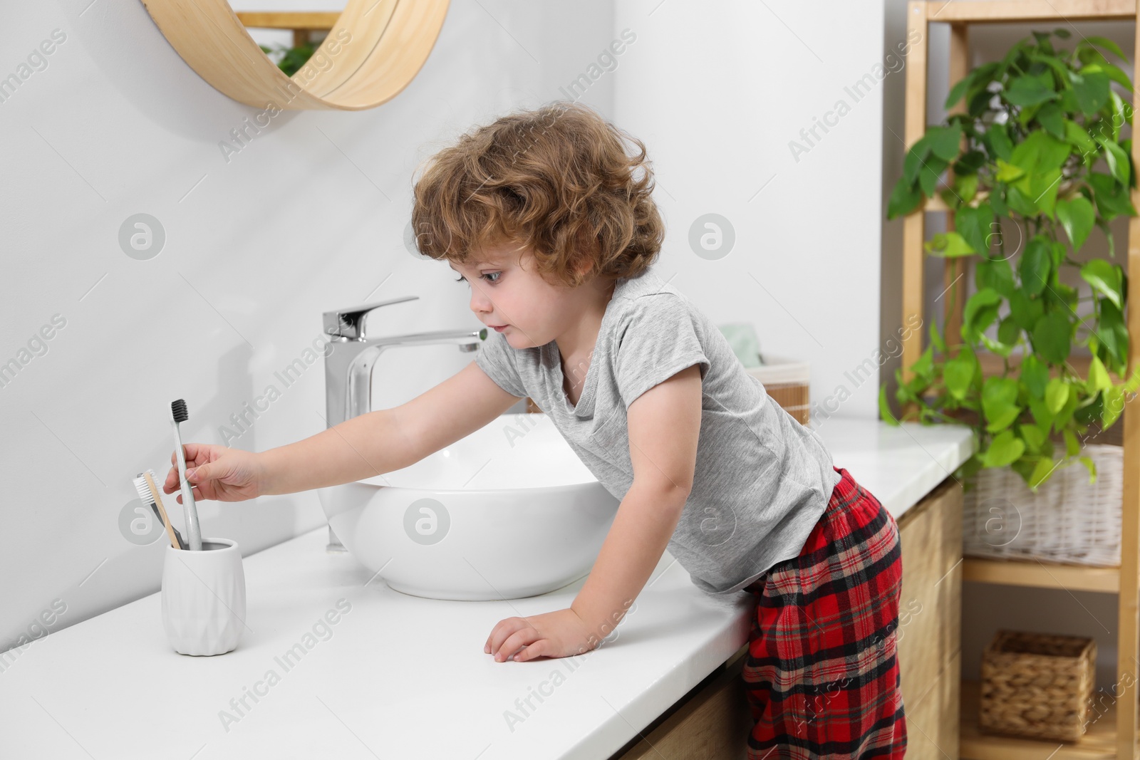 Photo of Little boy taking toothbrush from holder in bathroom