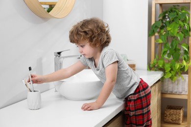 Little boy taking toothbrush from holder in bathroom