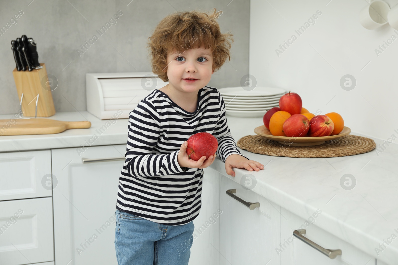 Photo of Little boy with red apple in kitchen