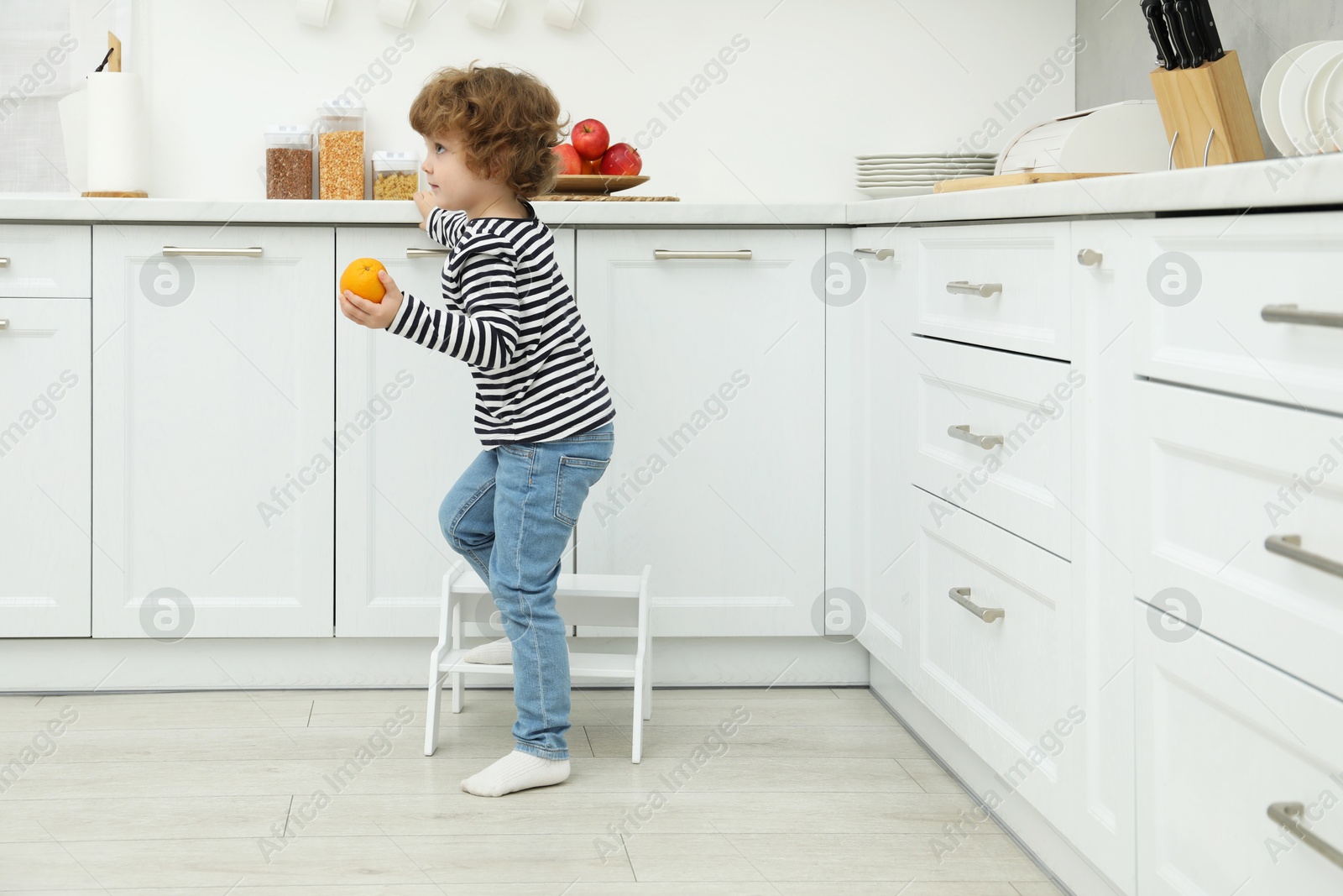 Photo of Little boy with orange standing on step stool in kitchen