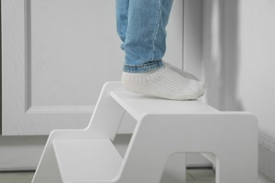 Photo of Little boy standing on step stool in kitchen, closeup