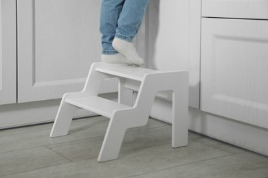 Photo of Little boy standing on step stool in kitchen, closeup