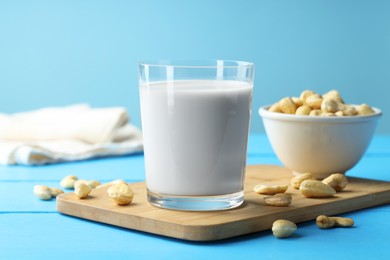 Photo of Fresh cashew milk in glass and nuts on light blue wooden table, closeup