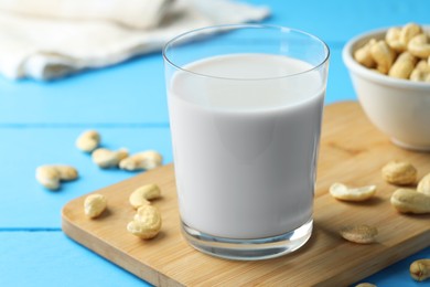 Fresh cashew milk in glass and nuts on light blue wooden table, closeup