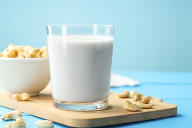 Photo of Fresh cashew milk in glass and nuts on light blue wooden table, closeup