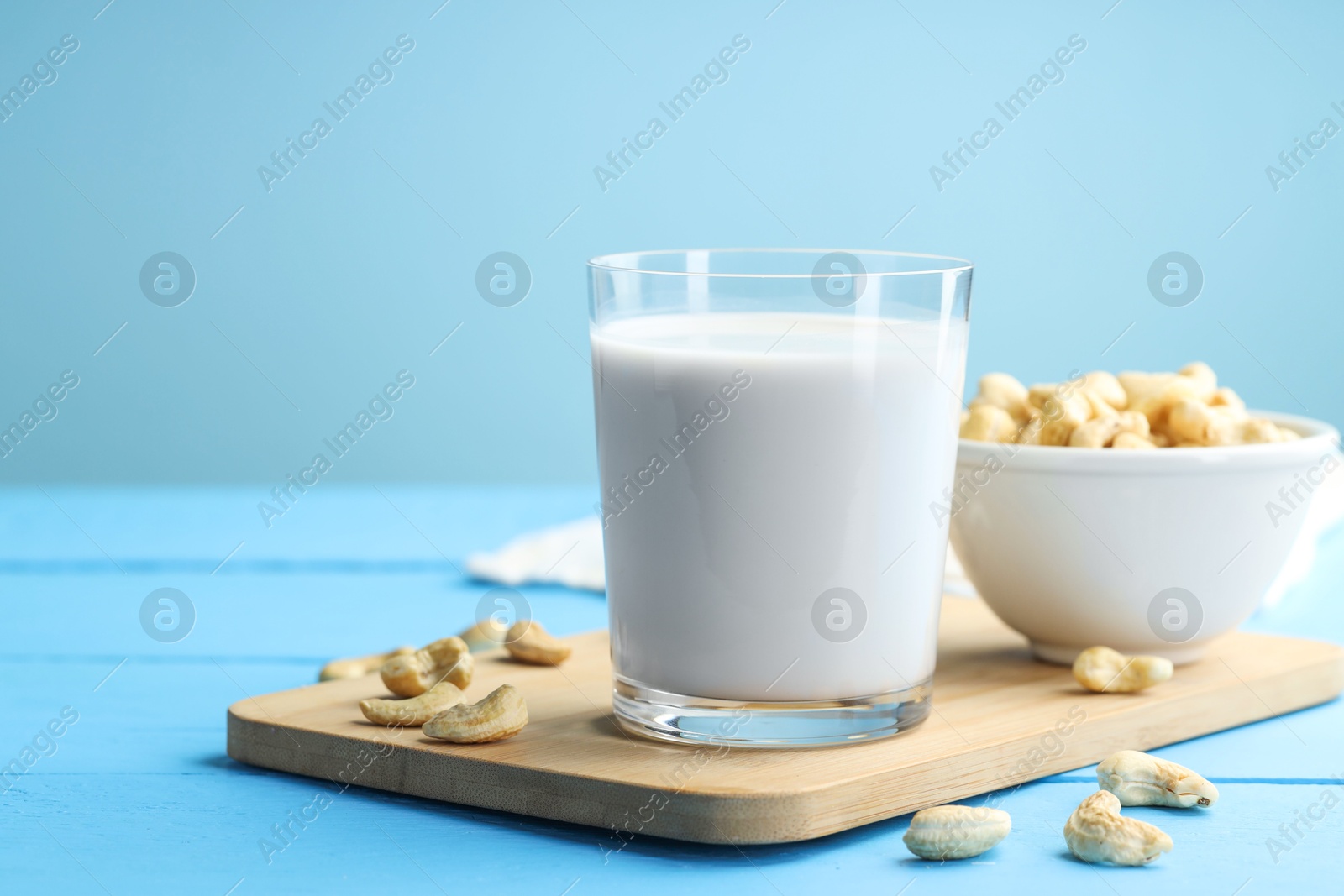 Photo of Fresh cashew milk in glass and nuts on light blue wooden table, closeup