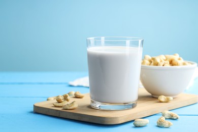 Fresh cashew milk in glass and nuts on light blue wooden table, closeup