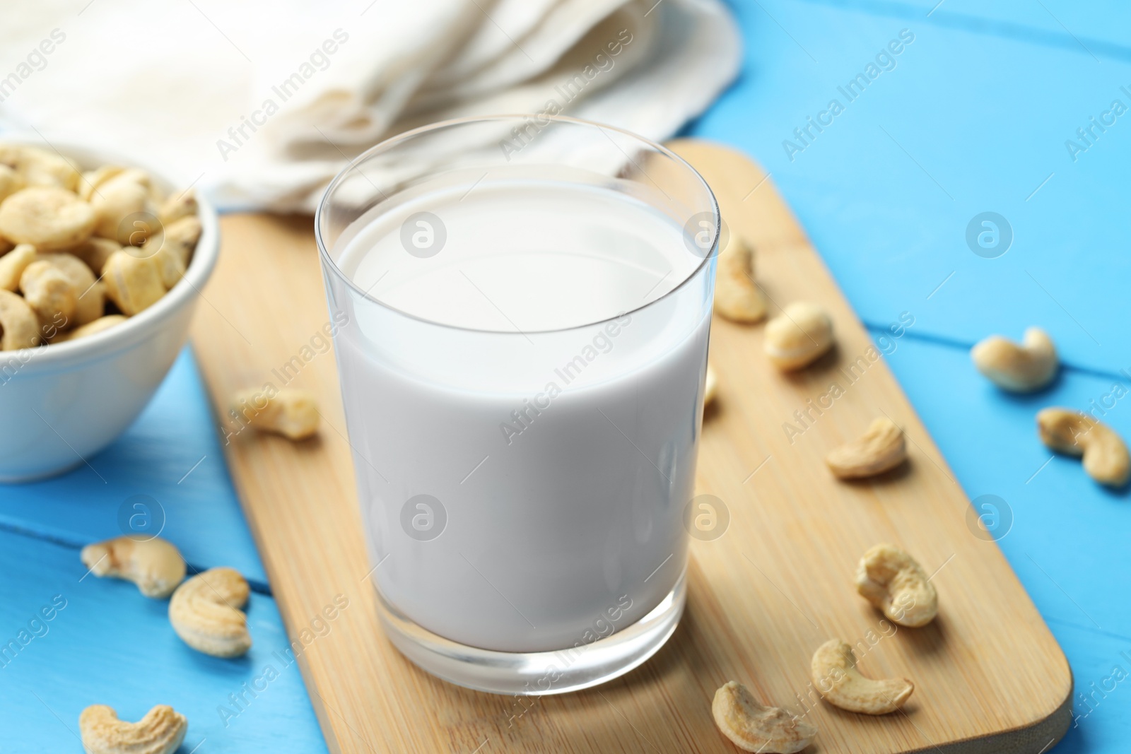 Photo of Fresh cashew milk in glass and nuts on light blue wooden table, closeup