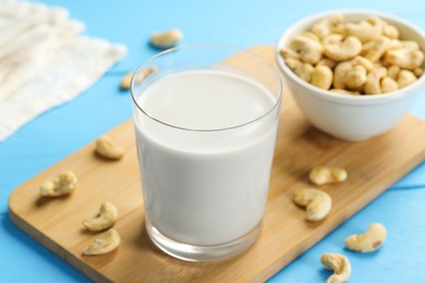 Photo of Fresh cashew milk in glass and nuts on light blue wooden table, closeup