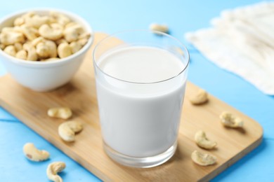 Photo of Fresh cashew milk in glass and nuts on light blue wooden table, closeup