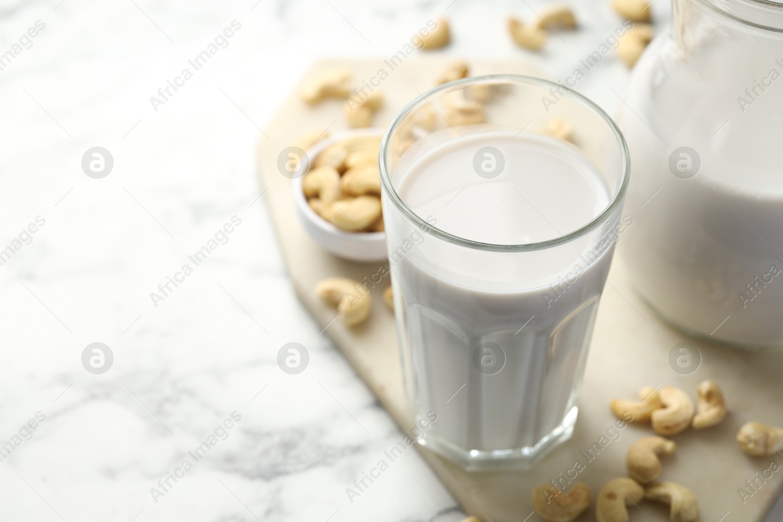 Photo of Fresh cashew milk in glass and nuts on white marble table, closeup. Space for text