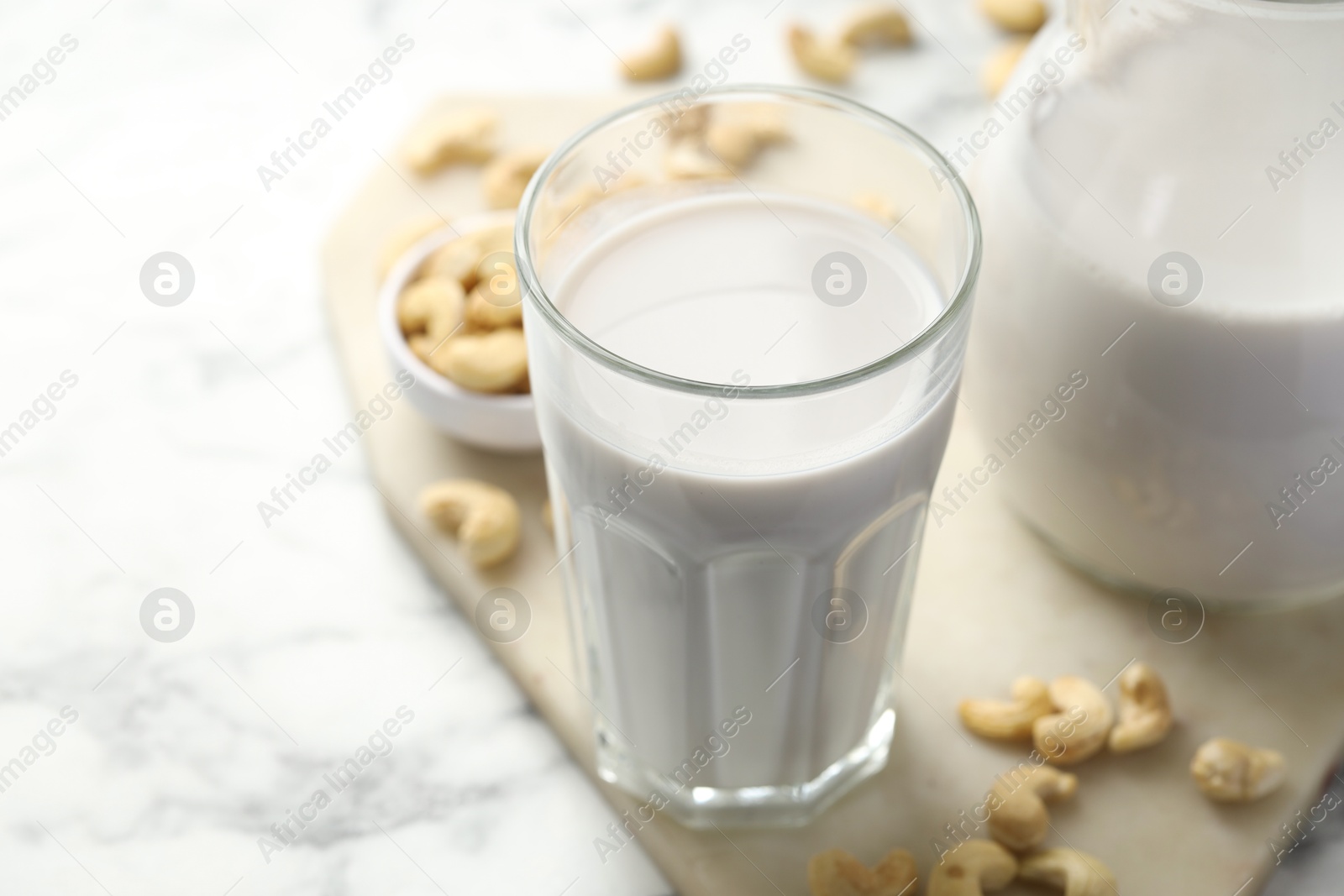 Photo of Fresh cashew milk in glass and nuts on white marble table, closeup. Space for text