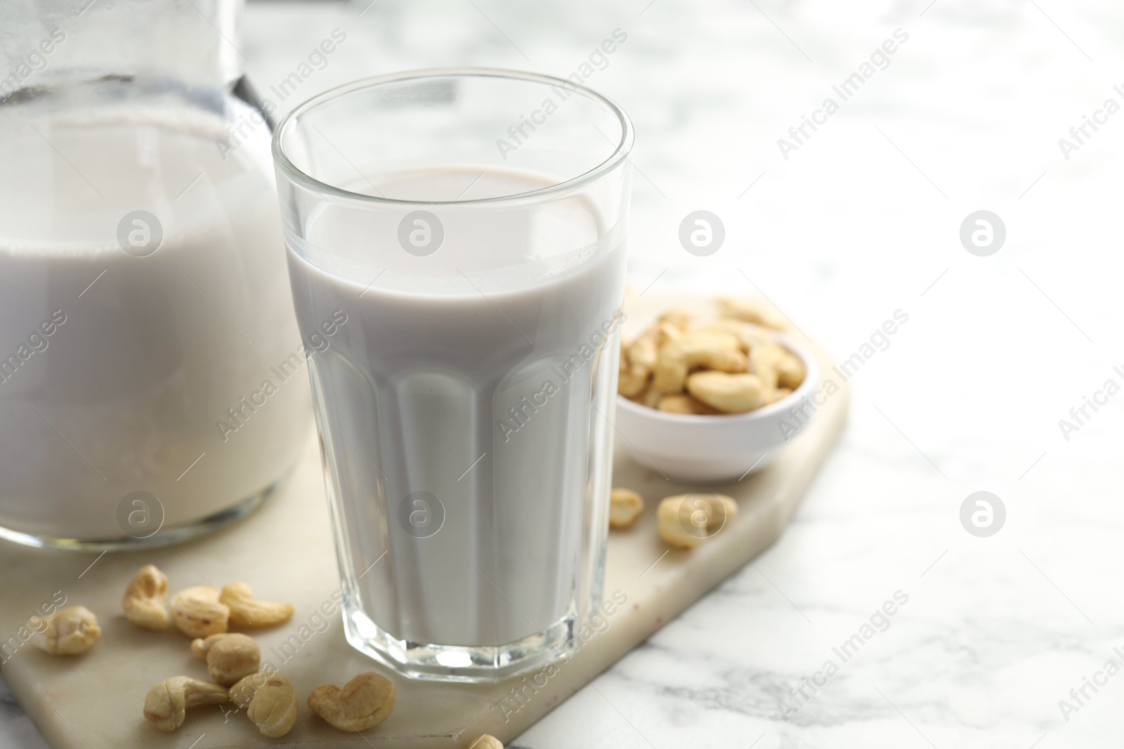 Photo of Fresh cashew milk in glass and nuts on white marble table, closeup. Space for text