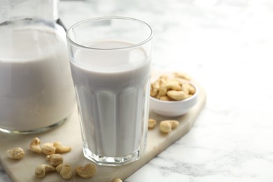 Photo of Fresh cashew milk in glass and nuts on white marble table, closeup. Space for text