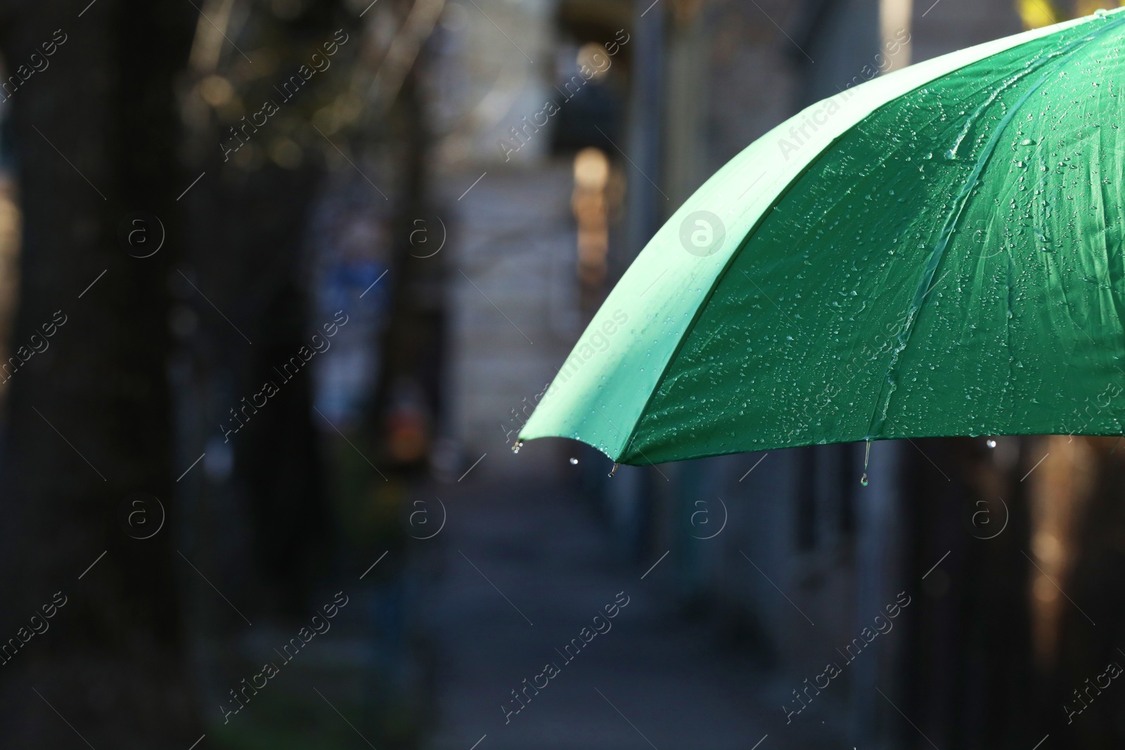 Photo of Open green umbrella under pouring rain outdoors, closeup. Space for text