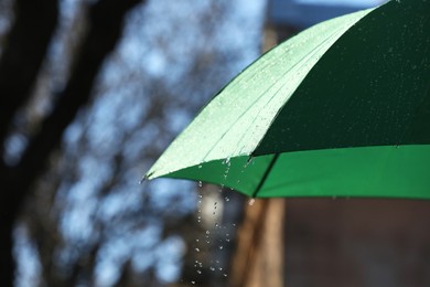 Photo of Open green umbrella under pouring rain outdoors, closeup