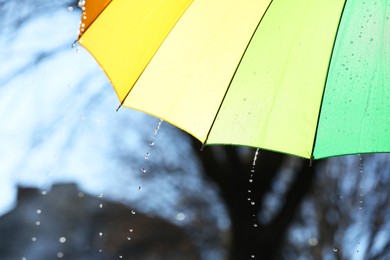 Photo of Open bright umbrella under pouring rain outdoors, closeup