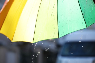 Photo of Open bright umbrella under pouring rain outdoors, closeup