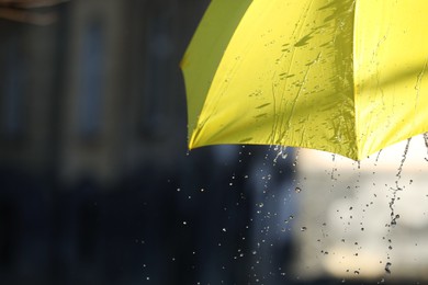 Photo of Open yellow umbrella under pouring rain outdoors, closeup. Space for text