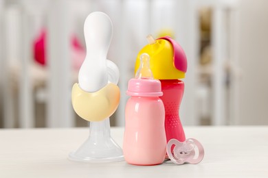 Photo of Feeding bottles with milk, breast pump and pacifier on white table indoors