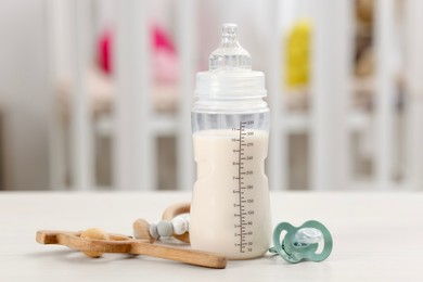 Photo of Feeding bottle with baby formula, pacifier and toys on white table indoors