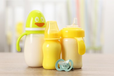 Photo of Feeding bottles with milk and pacifier on wooden table indoors