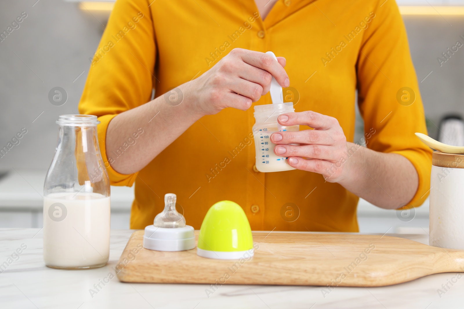 Photo of Mother making baby formula in feeding bottle at table indoors, closeup